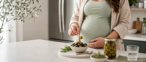 Bowl of green and black olives with a sealed jar and clean spoon on a calm kitchen counter.