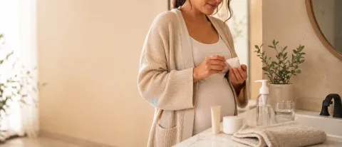 Pregnant person reviewing a simple skincare product beside a bathroom vanity with gentle acne-care items.