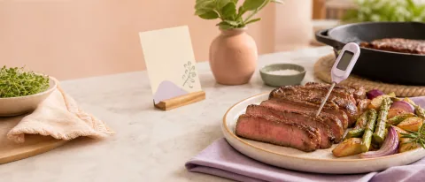 Kitchen scene with sliced steak, vegetables, and a food thermometer checking the internal temperature.